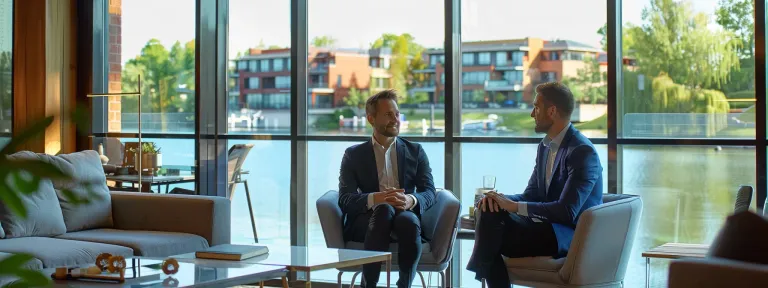 business professionals engage in a strategic discussion in a modern office overlooking luxury lakefront homes.